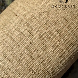 May include: Close-up of a rolled-up, woven material in a natural beige color. The texture is a tight, cross-hatched pattern. The text "BOUCRAFT ECO HANDICRAFT" is printed in black.