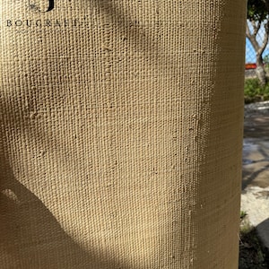 May include: Close-up of a rolled, textured, beige woven material. The material has a consistent pattern of vertical and horizontal lines, creating a grid-like appearance. The logo "BOUCRAFT" is visible in the upper left corner.