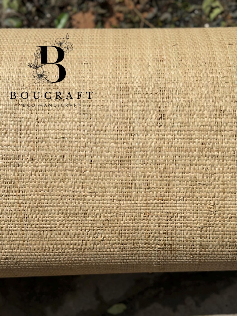 May include: Close-up of a roll of woven material in a natural beige color. The material has a textured, basket-weave pattern. The brand name "BOUCRAFT ECOHANDICRAFT" is printed in black, with a stylized "B" and floral design.