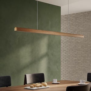 Puede incluir: Una lámpara colgante rectangular de madera moderna sobre una mesa de comedor. La lámpara tiene un acabado de madera natural y emite un brillo suave. La mesa del comedor está decorada con sillas, tazas y una bandeja con pasteles. La lámpara mide unos 120 cm de largo.