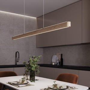 Könnte beinhalten: Moderne Küche mit einer rechteckigen Pendelleuchte aus Holz. Das Licht hängt über einem weißen Esstisch mit Gedecken. Braune Stühle und dunkle Arbeitsplatten ergänzen das neutrale Farbschema. Ein schwarzer Wasserhahn und Geräte sind sichtbar.