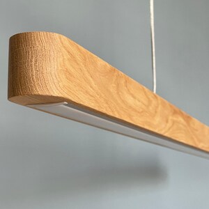 Large handmade wooden linear chandelier with LED lighting, rustic modern pendant light hanging above dining table, natural wood suspension lamp for farmhouse or modern interior.