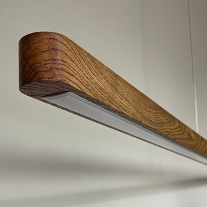 Minimalist wooden pendant lighting with LED, linear handmade chandelier suspended over dining room table, modern rustic ceiling light fixture made of natural wood.