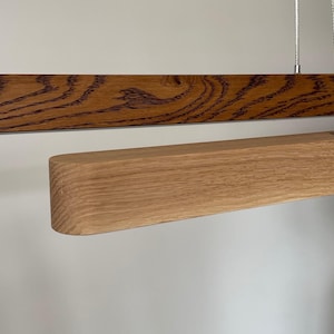 Modern linear wood pendant light in two-tone oak finish — dark and natural oak. Minimalist handcrafted LED chandelier for dining room or kitchen island in Japandi interior.