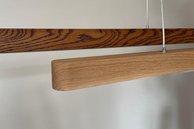 Modern linear wood pendant light in two-tone oak finish — dark and natural oak. Minimalist handcrafted LED chandelier for dining room or kitchen island in Japandi interior.