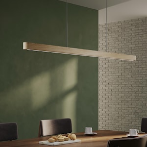Peut inclure: Un luminaire suspendu rectangulaire en bois moderne est suspendu au-dessus d'une table à manger en bois foncé. La lumière est suspendue par de fins fils contre un mur vert et un mur de briques. La table a des chaises et des couverts.
