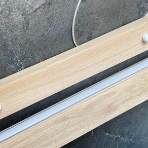 Close-up of light oak linear pendant light with matte acrylic diffuser and minimal mounting system. Scandinavian-style handmade wooden LED chandelier for dining or kitchen.