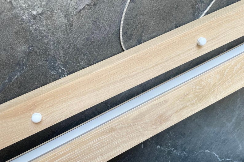 Close-up of light oak linear pendant light with matte acrylic diffuser and minimal mounting system. Scandinavian-style handmade wooden LED chandelier for dining or kitchen.