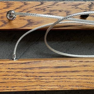 Close-up of dark oak wood grain and stainless steel suspension cables. Detail view of handcrafted linear pendant light with premium materials and durable construction