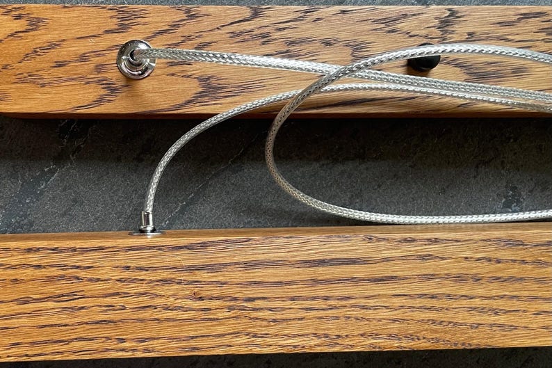 Close-up of dark oak wood grain and stainless steel suspension cables. Detail view of handcrafted linear pendant light with premium materials and durable construction