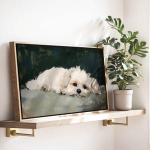 May include: A framed canvas art print featuring a white dog lying down. The dog has a fluffy coat and dark eyes. The background is a dark green color. The frame is made of light-colored wood. The artwork is displayed on a wooden shelf.