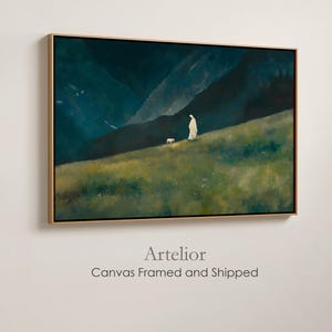 May include: A framed canvas art print depicts a figure in white clothing with a sheep on a grassy hillside, set against a backdrop of dark mountains and a twilight sky. The artwork is framed in a gold-colored border.