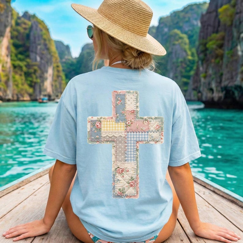 K&ouml;nnte beinhalten: Hellblaues T-Shirt mit einem Patchwork-Kreuz-Design auf dem R&uuml;cken. Das Kreuz besteht aus verschiedenen floralen und gemusterten Stoffen in Pastellfarben. Die Person tr&auml;gt einen Strohhut und eine Sonnenbrille und sitzt in einem Boot.