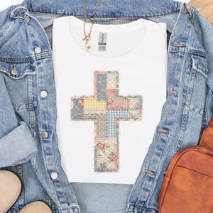 K&ouml;nnte beinhalten: Wei&szlig;es T-Shirt mit einem Patchwork-Kreuz-Design. Das Kreuz besteht aus verschiedenen Stoffmustern, darunter Blumenmuster, Vichy-Karo und Spitze, in Pastellfarben. Das T-Shirt ist mit einer Jeansjacke und einer braunen Ledertasche &uuml;berlagert.