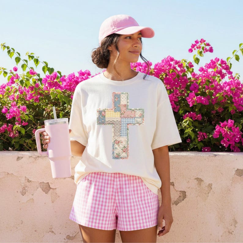 K&ouml;nnte beinhalten: Cremefarbenes T-Shirt mit einem Patchwork-Kreuz-Design in Pastellfarben. Die Person tr&auml;gt eine rosa Baseballkappe und eine rosa-wei&szlig; karierte Shorts. Ein rosa Becher mit Strohhalm wird in der linken Hand gehalten. Der Hintergrund zeigt leuchtend rosa Blumen.
