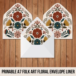 May include: White A7 envelope with a floral folk art design. The design features a large rust-colored flower surrounded by teal, yellow, and pink flowers and green leaves. The text at the bottom reads "PRINTABLE A7 FOLK ART FLORAL ENVELOPE LINER."