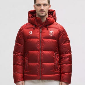 Pode incluir: Casaco acolchoado vermelho com capuz e zíper completo. O casaco apresenta um logotipo branco no peito esquerdo e o logotipo da equipa olímpica canadiana no direito. Casaco de inverno quente.