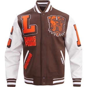 Op de afbeelding: Bruin en witte varsity jas met oranje accenten. Voorzien van de letter "L" en de woorden "DAWG POUND" in oranje. De jas heeft witte mouwen en een bulldoglogo. Het nummer "1" staat op de rechter mouw. Het woord "BROWNS" is ook zichtbaar.