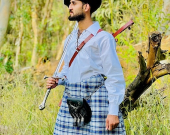 Peut inclure: Tenue écossaise traditionnelle avec un kilt à carreaux bleus et blancs, une chemise blanche et un chapeau noir. Une épée est tenue dans une main, et une sangle en cuir avec un fourreau d'épée est portée sur la poitrine. Un sporran en cuir noir est suspendu au kilt.
