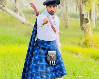 Peut inclure: Une personne vêtue d'un costume traditionnel écossais, tenant une épée. Le kilt est bleu avec un motif à carreaux noirs. La tenue comprend une chemise blanche, un béret noir et un sporran en cuir. La personne se tient dans un champ herbeux.