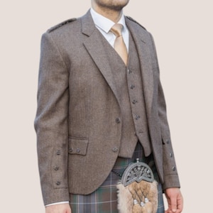 May include: A brown tweed three-piece suit, including a jacket, waistcoat, and trousers. The jacket features a notched lapel and buttoned cuffs. The waistcoat has a button-down front. The suit is worn with a white shirt and a gold tie. A traditional Scottish kilt is also visible.