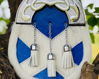 Puede incluir: Un sporran escocés azul y blanco para kilt con un adorno de metal plateado y tres borlas blancas.