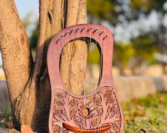 May include: A wooden lyre with intricate carvings of leaves and flowers. The lyre is brown and has a natural wood finish. It is resting on a bed of fallen leaves.