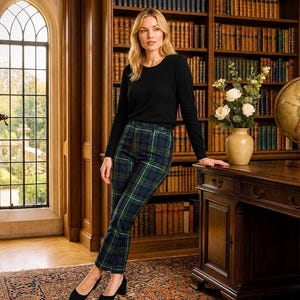 May include: A woman wearing a black long-sleeve shirt and plaid pants with a green, blue, and white pattern. She is wearing black heels. The background includes a wooden desk, a globe, a vase of flowers, and a bookshelf.
