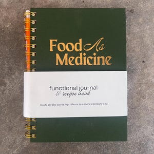 May include: A green spiral bound journal with gold rings. The cover has the text "Food As Medicine" in gold lettering and the words "functional journal & recipe book" in black lettering. The text "Inside are the secret ingredients to a more legendary you!" is printed in black lettering on a white label.