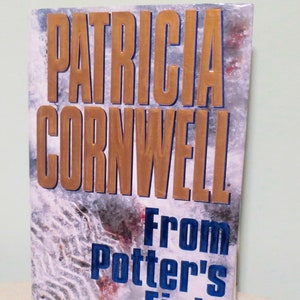 May include: A book by Patricia Cornwell, titled "From Potter's Field". The cover displays the author's name in gold, with the title in blue. The background has a textured, abstract design. The book is standing on a white surface.