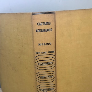 May include: A yellow book with the title "Captains Courageous" by Kipling. The book is published by Sun Dial Press and features a decorative black design on the spine.