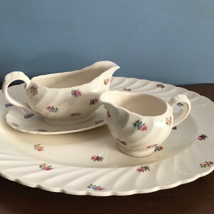 May include: A white ceramic serving set with a floral pattern. The set includes a large platter, a gravy boat with a matching saucer, and a small creamer.