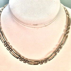 May include: A gold chain necklace with a geometric link design. The necklace is on a white mannequin bust.