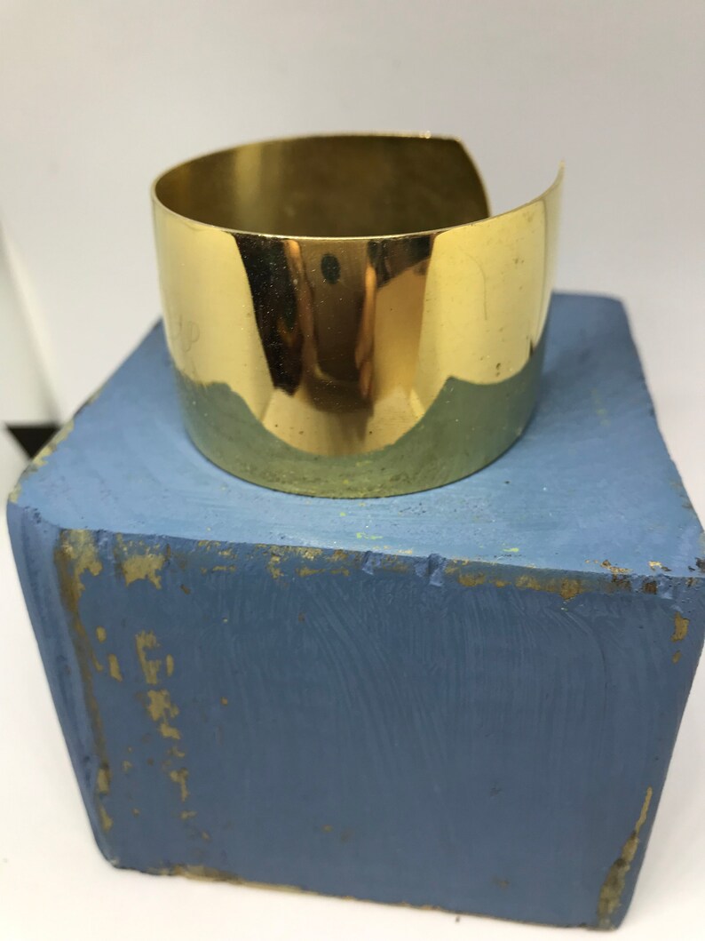 May include: A shiny gold metal cuff bracelet. The bracelet is wide and has a simple, rounded design.