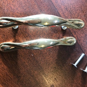 May include: Two gold-toned cabinet door pulls with a twisted design and two silver screws.