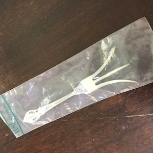May include: A silver serving fork with a decorative handle, packaged in a clear plastic bag with the text "LUNT STERLING" printed on the bag.