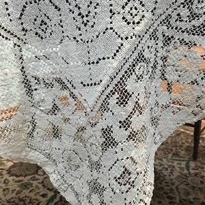 May include: White crocheted tablecloth with a delicate floral pattern. The tablecloth is made of fine lace and has a scalloped edge.