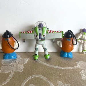 May include: Four Toy Story character figurines. Two Mr. Potato Head figures with black hats and blue bases, a Buzz Lightyear figure with wings extended, and a small Buzz Lightyear figure.