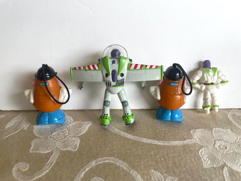 May include: Four Toy Story character figurines. Two Mr. Potato Head figures with black hats and blue bases, a Buzz Lightyear figure with wings extended, and a small Buzz Lightyear figure.