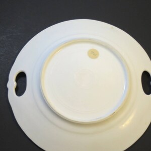 Puede incluir: Plato de servir de cer&aacute;mica blanca con dos asas. El plato tiene un borde elevado y un acabado liso y brillante. La parte inferior del plato tiene una peque&ntilde;a pegatina redonda con el n&uacute;mero "22" en ella.