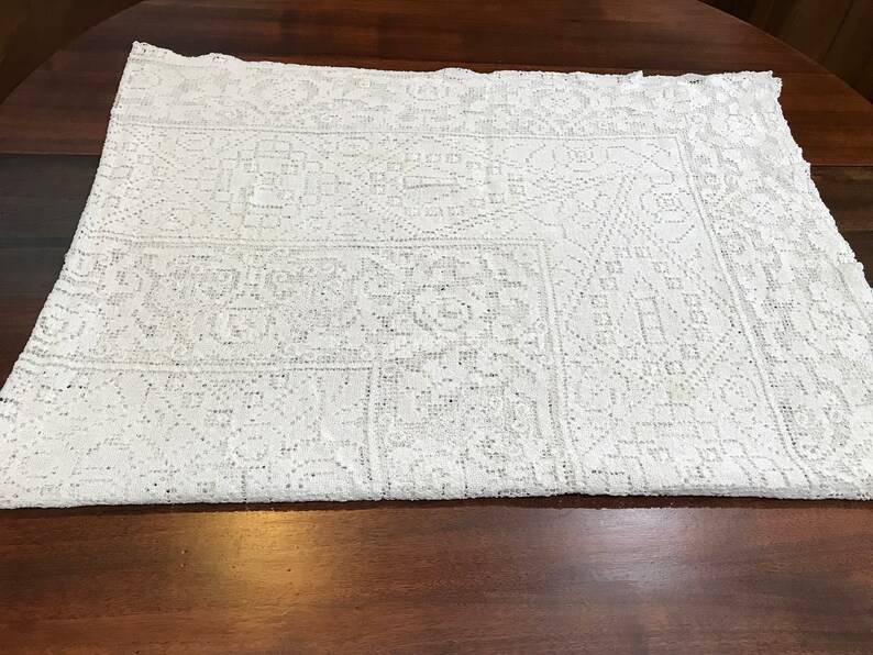 May include: White crocheted tablecloth with a geometric pattern. The tablecloth is folded in half and laid on a wooden surface.