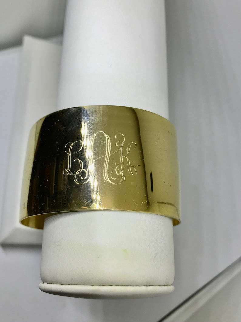 May include: A gold-toned metal cuff bracelet with the monogram "BAK" engraved on the front.