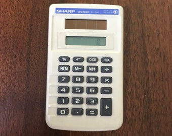 May include: A white Sharp EL-243 calculator with black buttons and a digital display. The calculator has a solar panel and a variety of function keys, including percentage, memory, and arithmetic operations. The calculator is on a wooden surface.