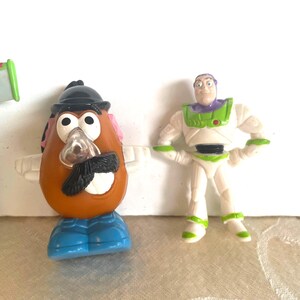 May include: Toy Story character figurines, including Mr. Potato Head with a black hat, mustache, and blue shoes, and Buzz Lightyear in a white and green spacesuit. The toys are plastic and brightly colored.