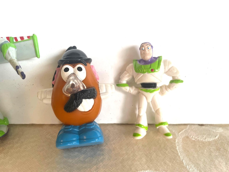 May include: Toy Story character figurines, including Mr. Potato Head with a black hat, mustache, and blue shoes, and Buzz Lightyear in a white and green spacesuit. The toys are plastic and brightly colored.