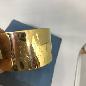 May include: A gold metal napkin ring with the initials "G.K." engraved on the front.