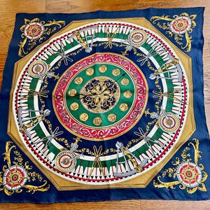 May include: Navy blue silk scarf with a detailed clock face design. The scarf features a central clock face with Roman numerals, surrounded by green, red, and gold accents. Decorative elements include compass-like designs and gold filigree.
