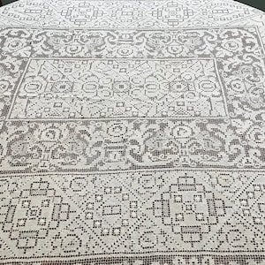 May include: A white tablecloth with a delicate, intricate lace pattern in a dark brown color. The pattern is geometric and symmetrical, with repeating motifs of squares, circles, and flowers.