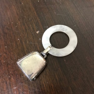 May include: A silver baby rattle with a bell and a white teething ring.