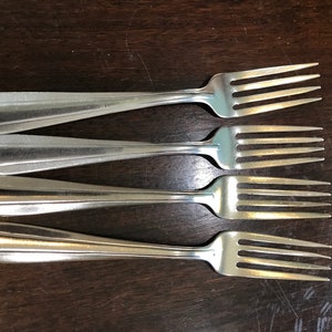 May include: Four silver forks with a simple design, laid out in a row on a wooden surface.